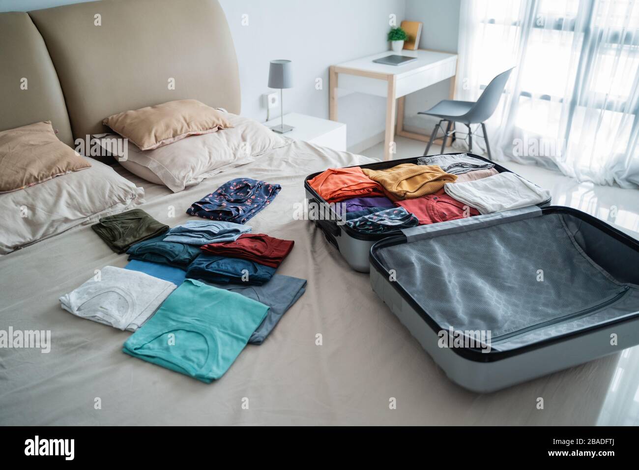 open suitcase with a lot of clothes on the bed in the bedroom Stock