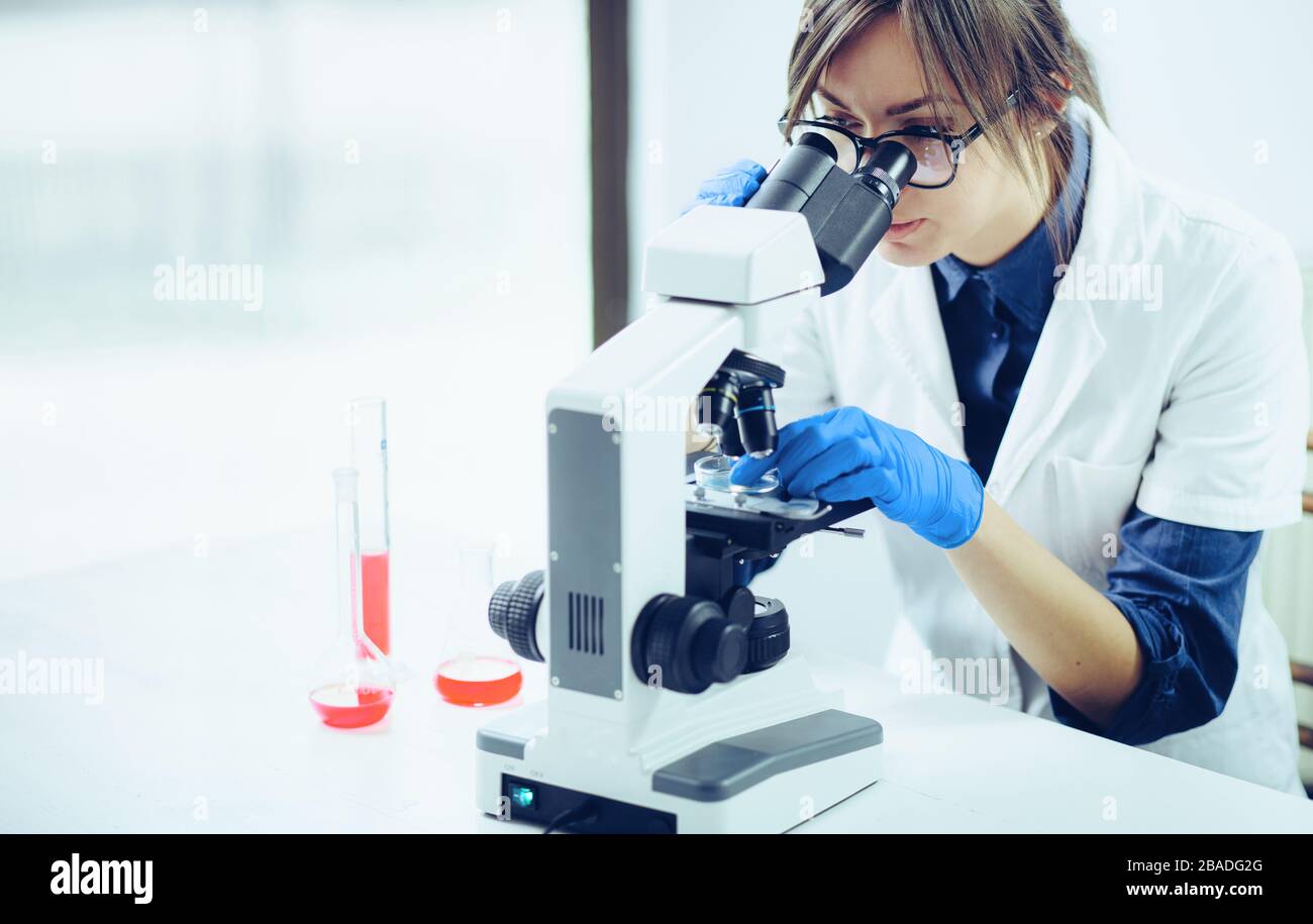 Young scientist looking through a microscope in a laboratory. Young scientist doing some research. Stock Photo