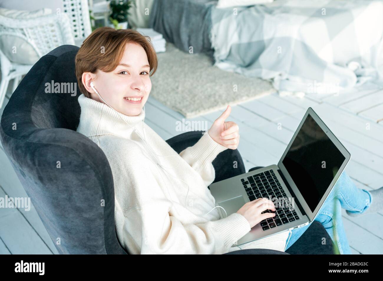 Smiling girl sits with laptop and holds thumbs up Stock Photo - Alamy