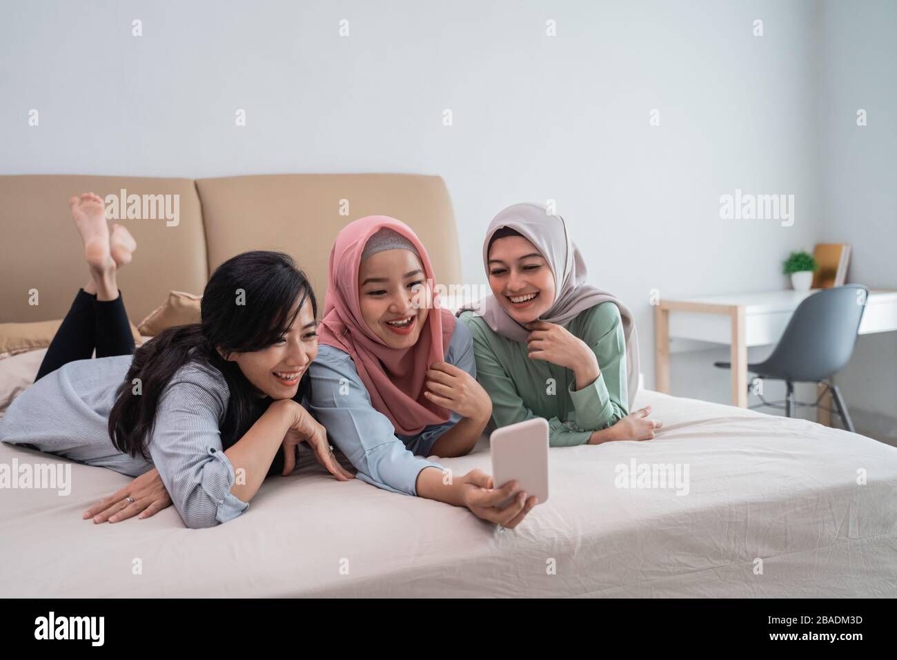 three Asian women lying in bed while doing video calls using a smartphone while enjoying a relaxing time Stock Photo