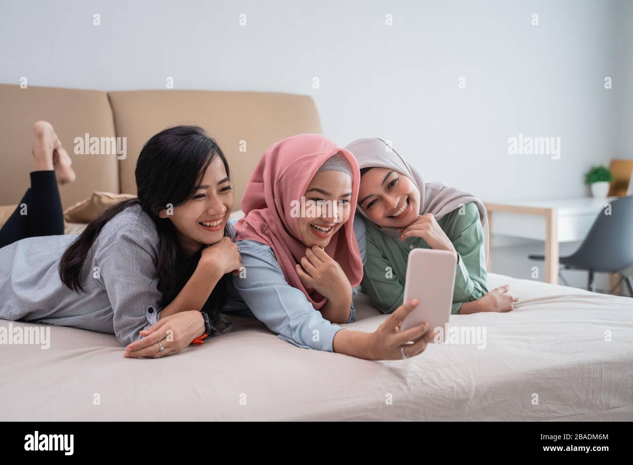 three Muslim women lying in bed while doing video calls using a smartphone while enjoying a relaxing time Stock Photo