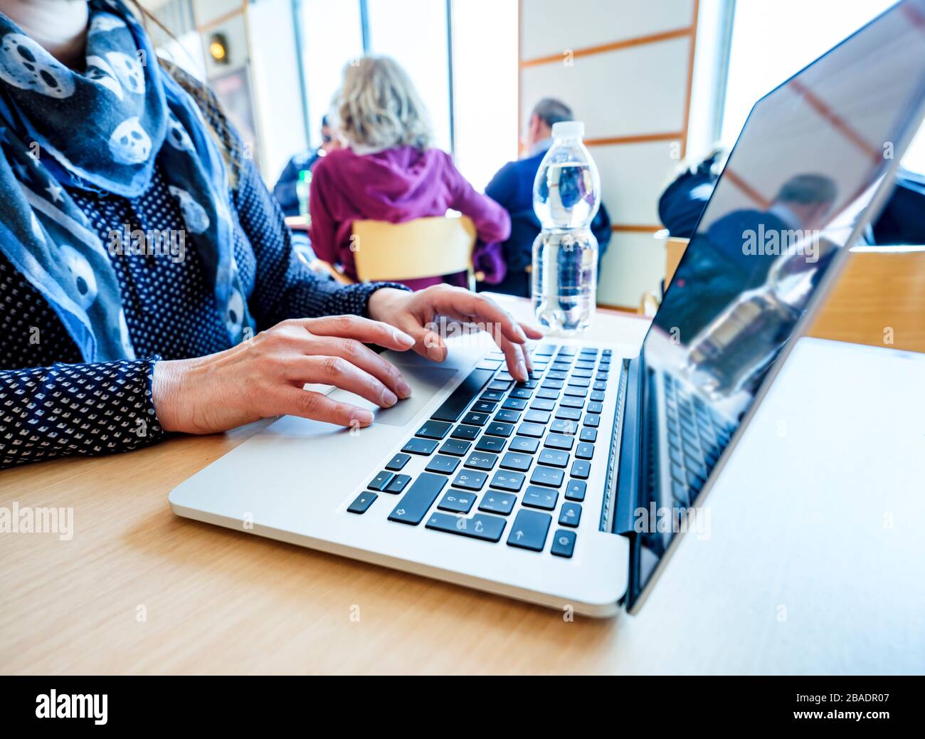 Woman using laptop, searching the web, browsing information while sitting at a table in a public place Stock Photo