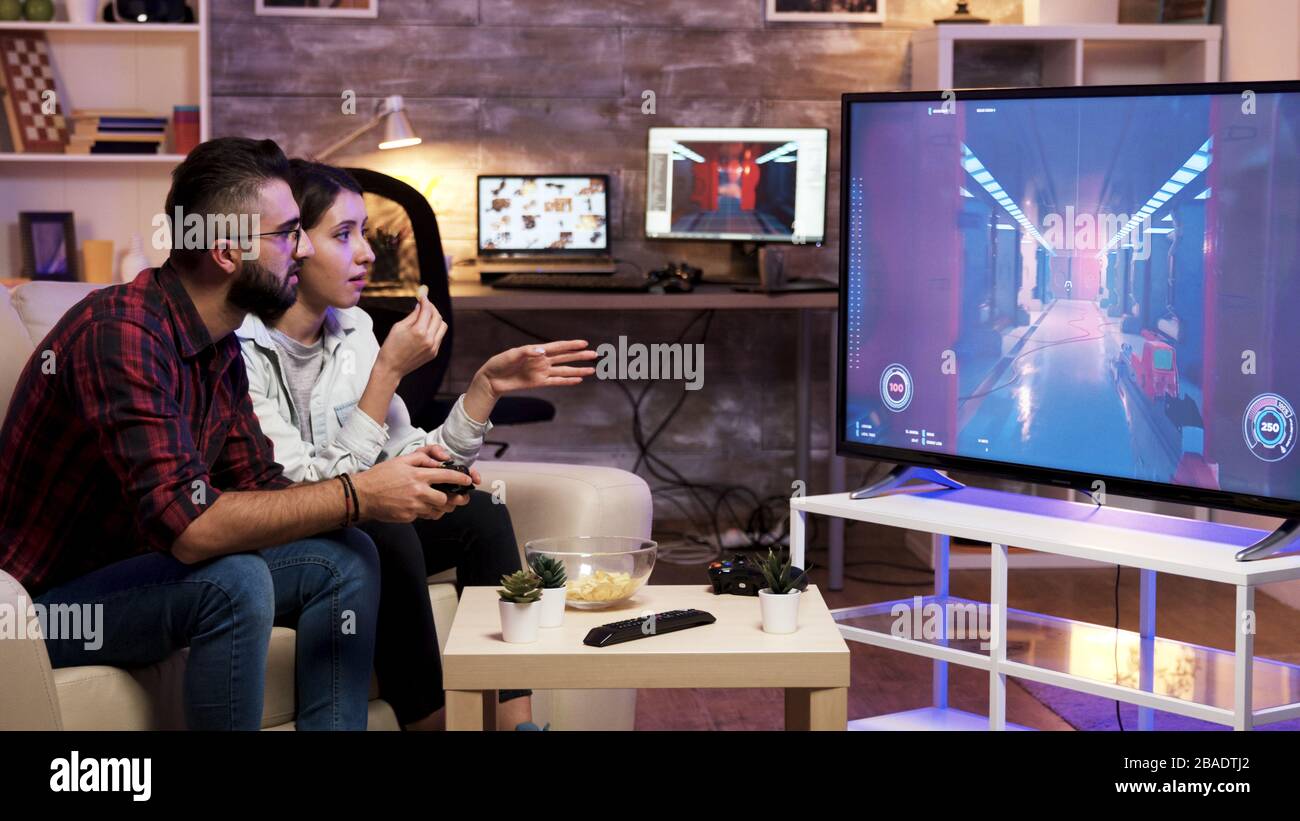 Man sitting on couch playing video games on television with girlfriend next to him. Stock Photo