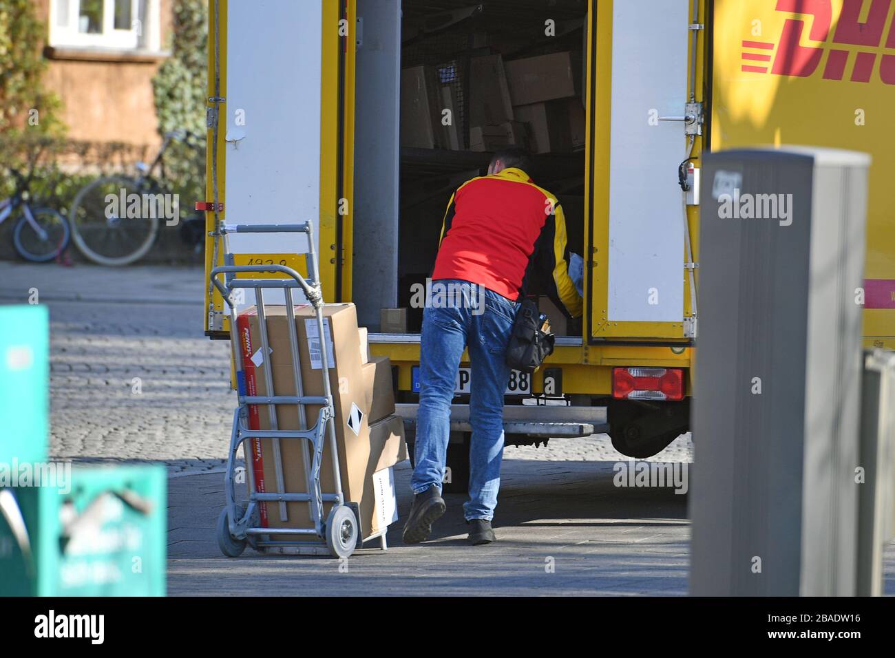 Munich, Deutschland. 26th Mar, 2020. DHL parcel deliverer, parcel carrier,  at work, unloads his parcel car, post bus, DHL, parcel, parcels, parcel  service, deliver, unload, deliver, transporter, hand truck. ? Sven Simon
