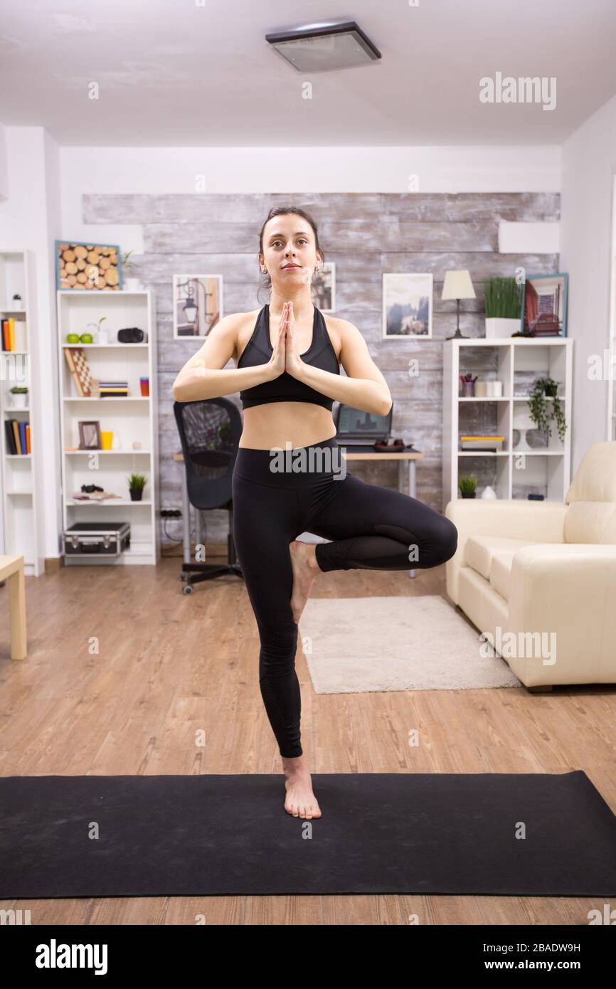 Smiling young woman while doing tree yoga pose wearing black sportwear ...