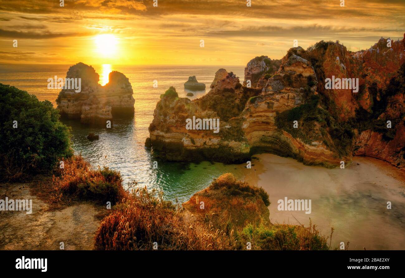 The scenic Camilo Beach in Lagos, Portugal, with its distinctive cliffs and the ocean in gold light at sunrise Stock Photo