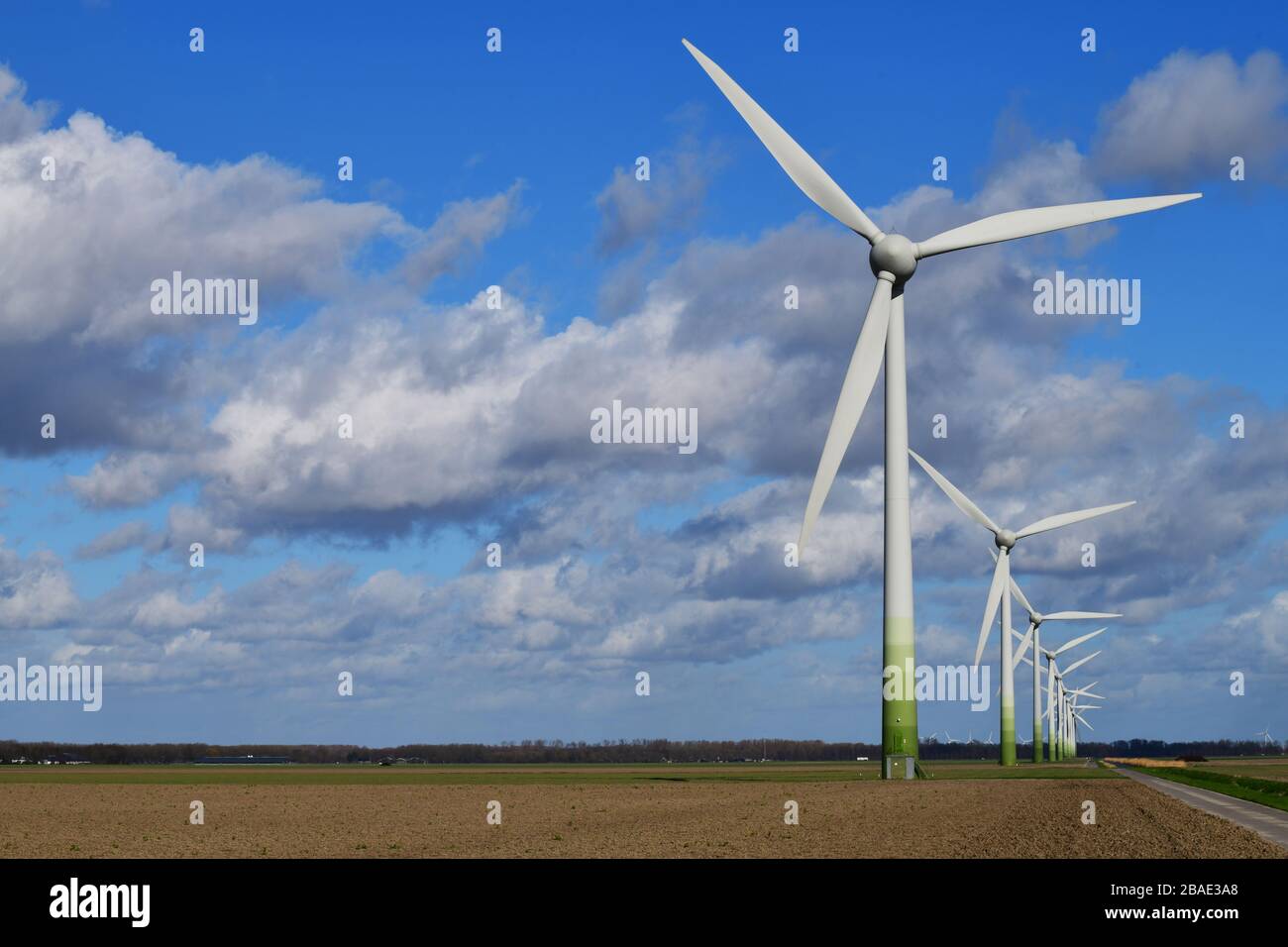 Line of modern windmills in typical Dutch agricultural landscape against blue sky with large white clouds Stock Photo