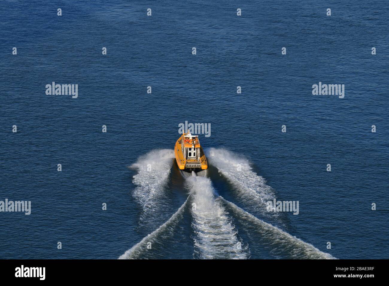Rear high angle view of bright yellow pilot boat speeding away leaving a wide wake in the water Stock Photo