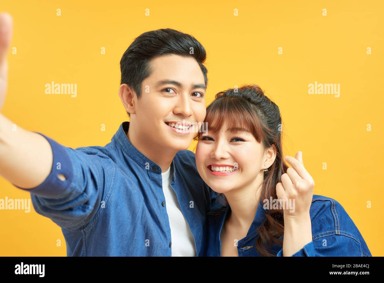 Self portrait of funny foolish cheerful adorable young cute couple smiling showing teeth, looking straight with opened mouths over yellow background, Stock Photo