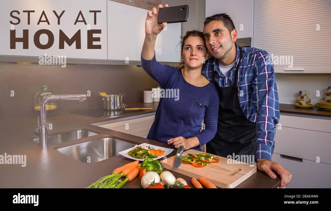 Couple in kitchen cooking and taking selfie with smartphone Stock Photo