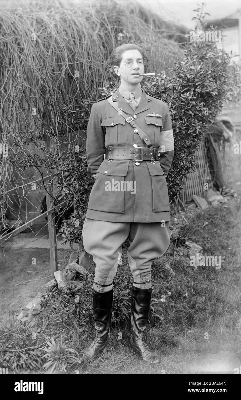 A vintage black and white photograph taken in 1917,  showing a young male pilot of the British Royal Flying Corps, during the First World War,  in full uniform wearing a monocle, and smoking a cigarette in a holder. Photo is taken in the garden of a private house in England. Stock Photo