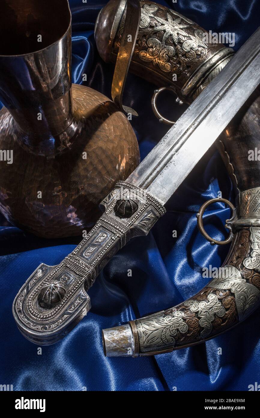 Beautiful example of caucasian dagger with silver powder flask on blue silk background. 19th century (Time of Russian-Caucasian wars (1816-1864)). Rus Stock Photo