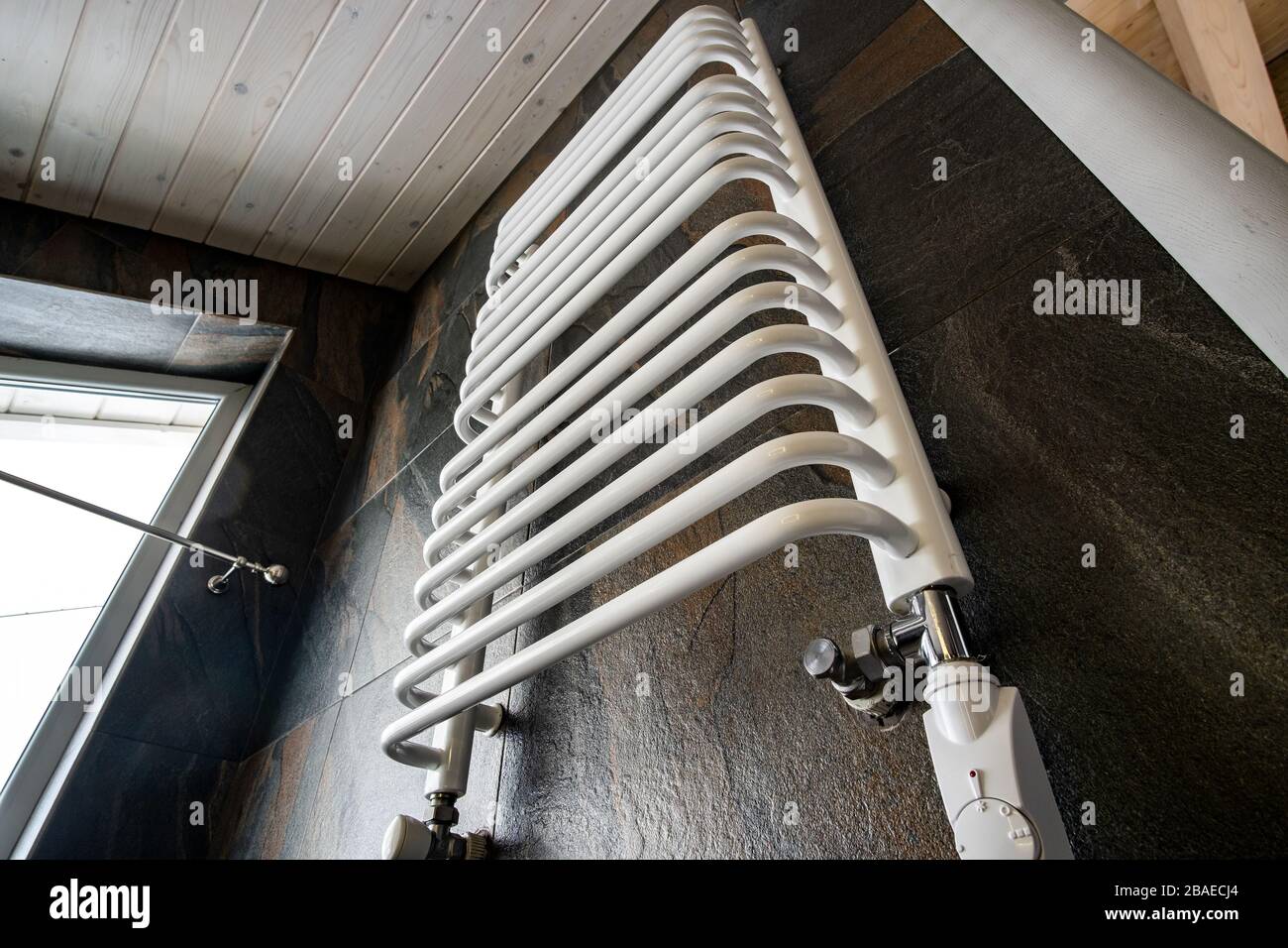 White contemporary electric towel dryer mounted on black tiled wall in