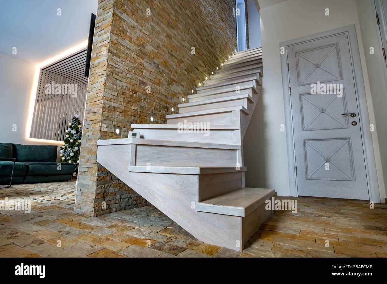 Stylish wooden contemporary staircase inside loft house interior. Modern hallway with decorative limestone brick walls and white oak stairs. Stock Photo