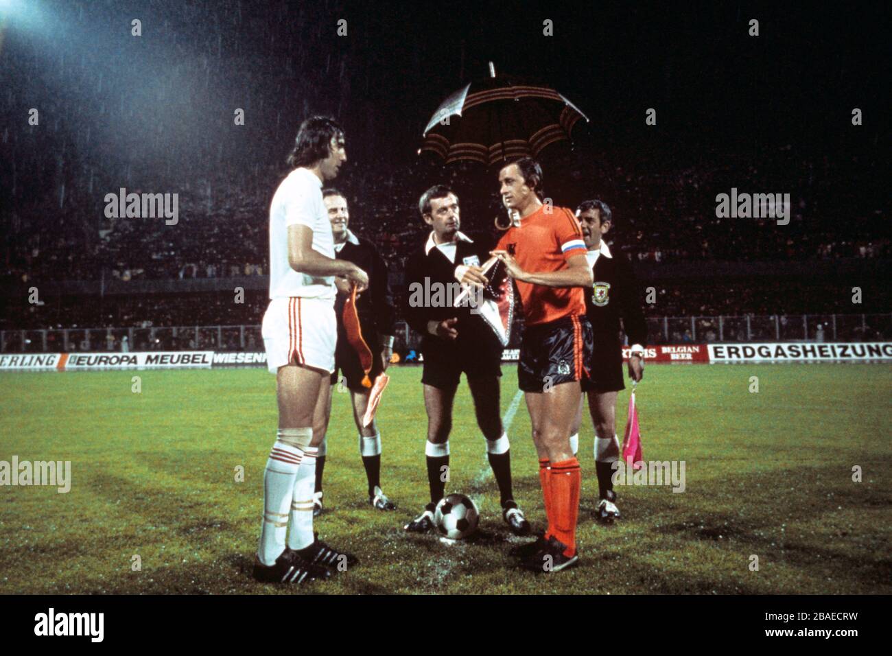 Referee Clive Thomas (c) holds an umbrella over Holland captain Johan Cruyff (r) as he exchanges pennants with Czechoslovakia captain Anton Ondrus (l) before the match Stock Photo