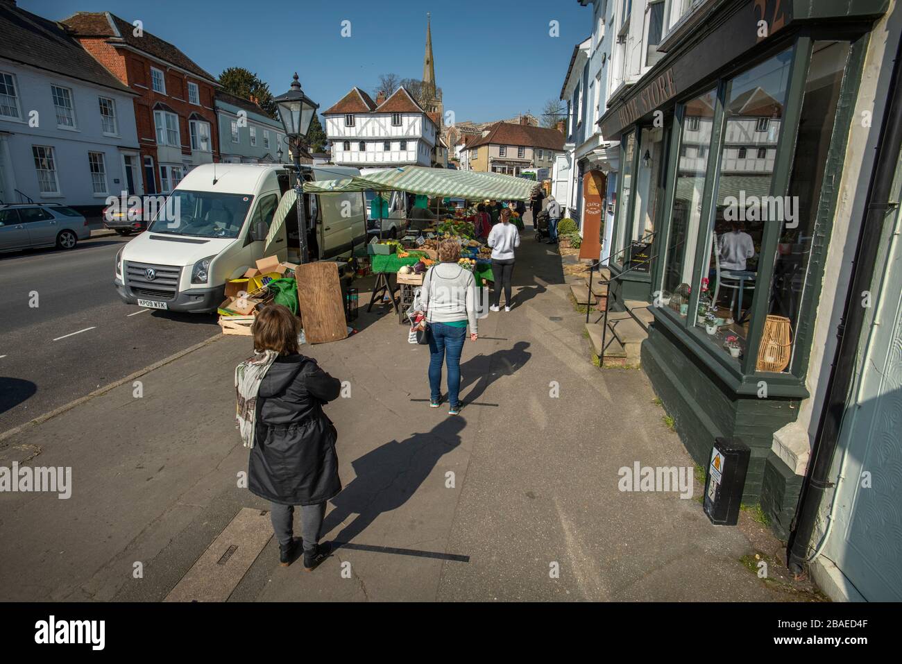 Thaxted, UK. 27th Mar, 2020. Thaxted Essex UK. Market day during Coronavirus lock down. 27 March 2020 Showing customers keeping the regulation two metres apart marked with black tape on the pavement waiting to be served queueing at the fruit and veg stall. Thaxted Market has existed for hundreds of years in the shadow of the 14th century Guildhall and Thaxted Church. Photograph by Credit: BRIAN HARRIS/Alamy Live News Stock Photo