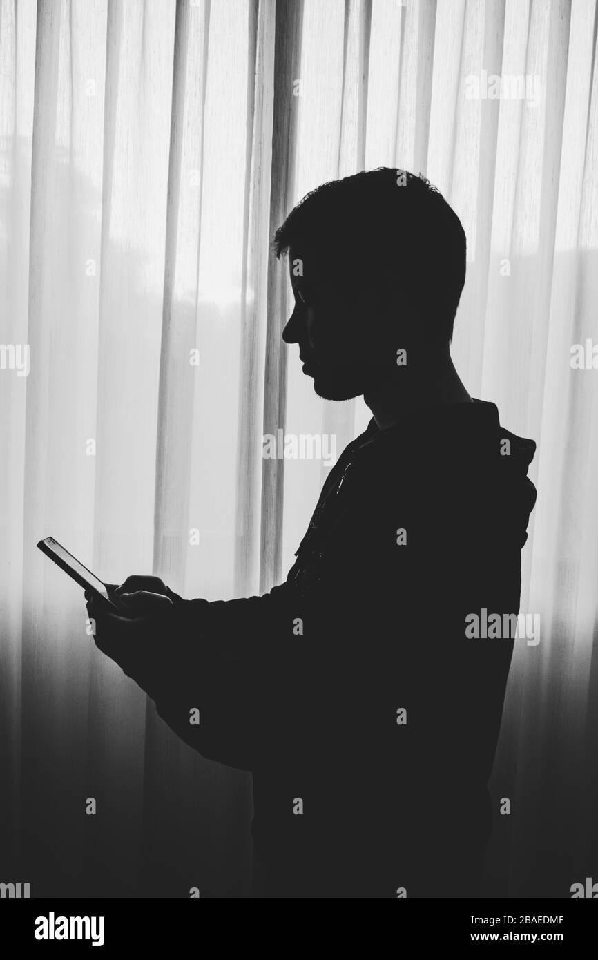 Side view of silhouette of boy standing by the window using a mobile phone Stock Photo