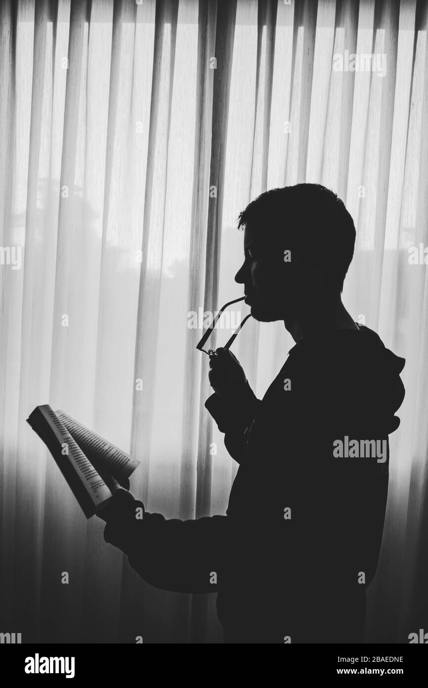 Side view of silhouette boy standing by window reading a book Stock Photo