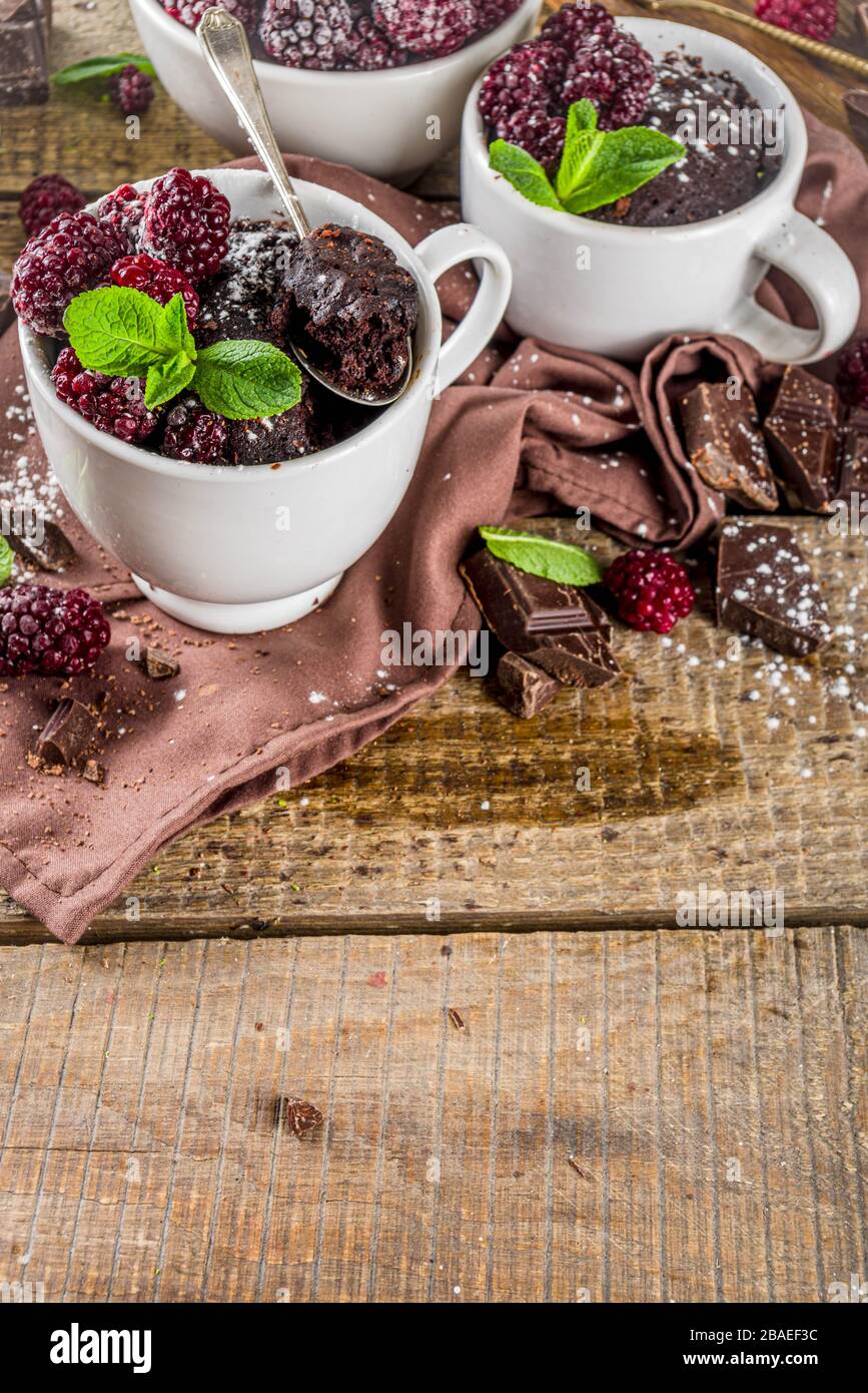 Homemade chocolate mug cake with blackberry. Breakfast easy snack recipe, chocolate non dairy cake in mugs, with blackberry, sugar powder and mint, wo Stock Photo
