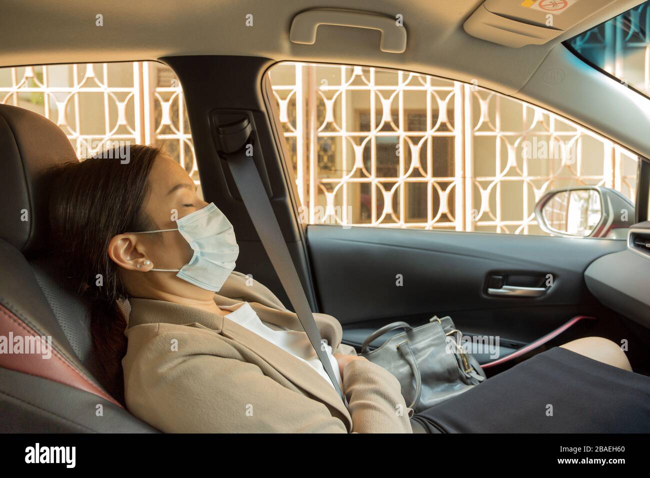 Asian businesswoman with protective mask laying sleeping in car. Stock Photo