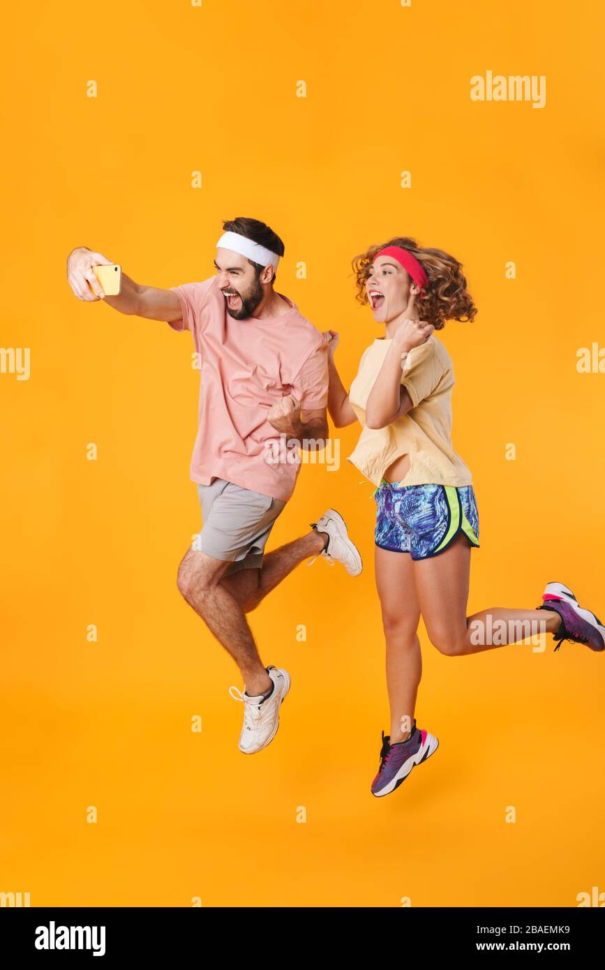 Portrait of athletic young couple wearing headbands smiling and taking selfie photo on cellphone isolated over yellow background Stock Photo