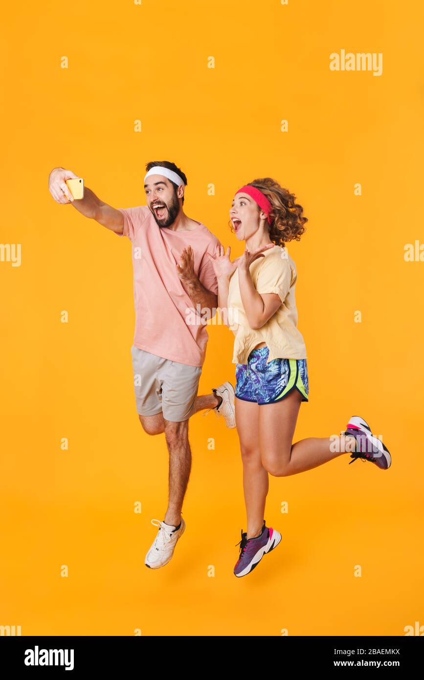 Portrait of athletic young couple wearing headbands smiling and taking selfie photo on cellphone isolated over yellow background Stock Photo