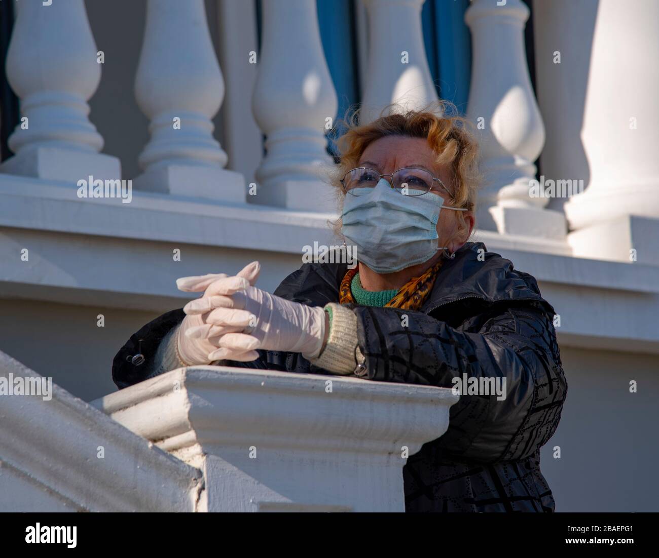An elderly woman in rubber gloves and a protective mask stands against ...