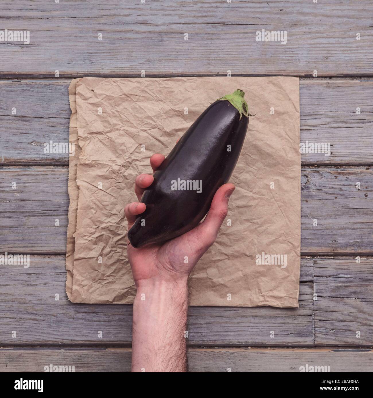 A male hand holding a fresh aubergine against a rustic background Stock Photo