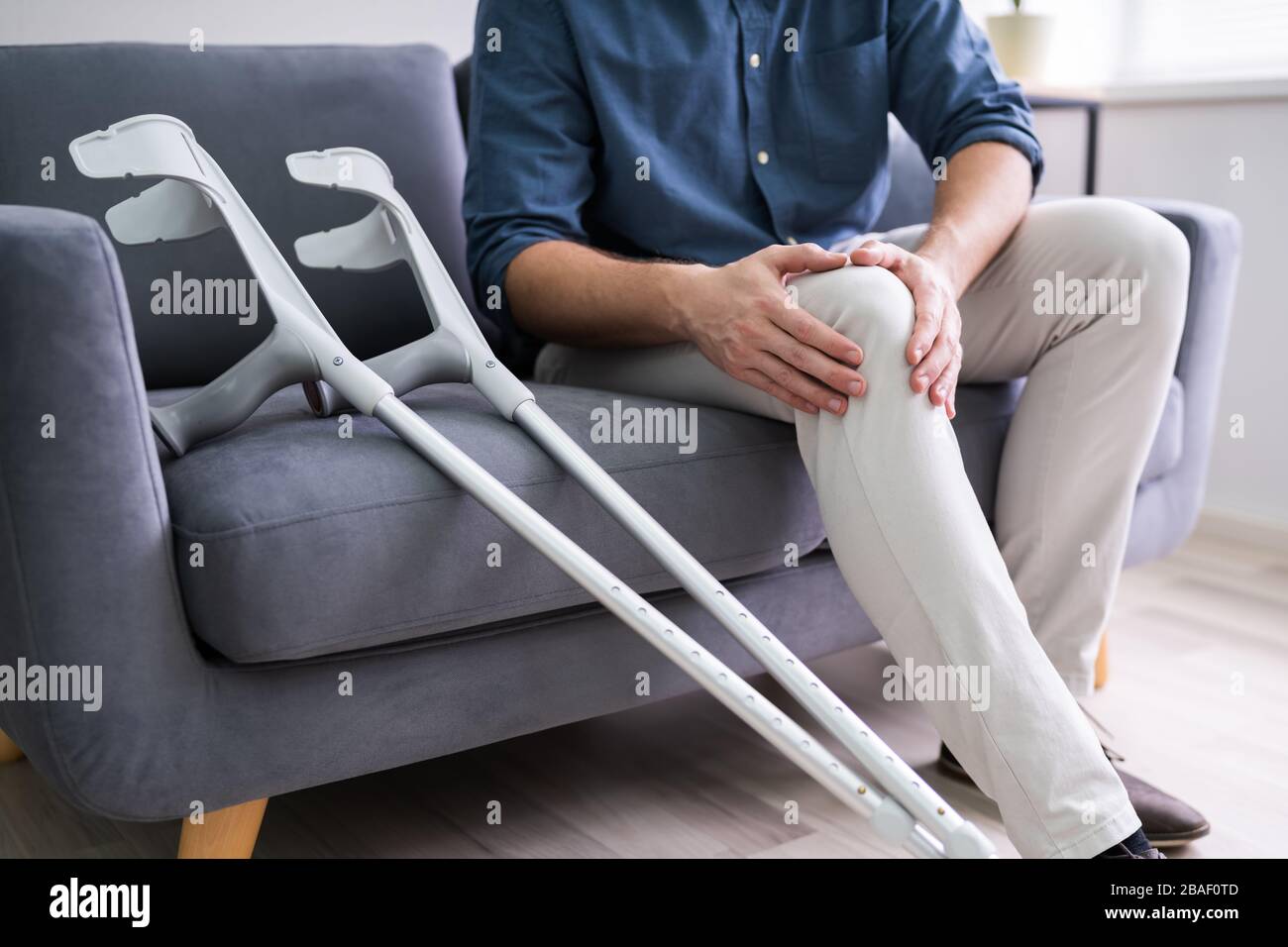 Man Suffering From Knee Pain Sitting On Sofa Stock Photo