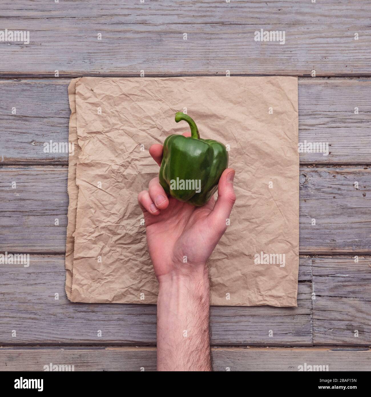 A male hand holding a fresh pepper against a rustic background Stock Photo