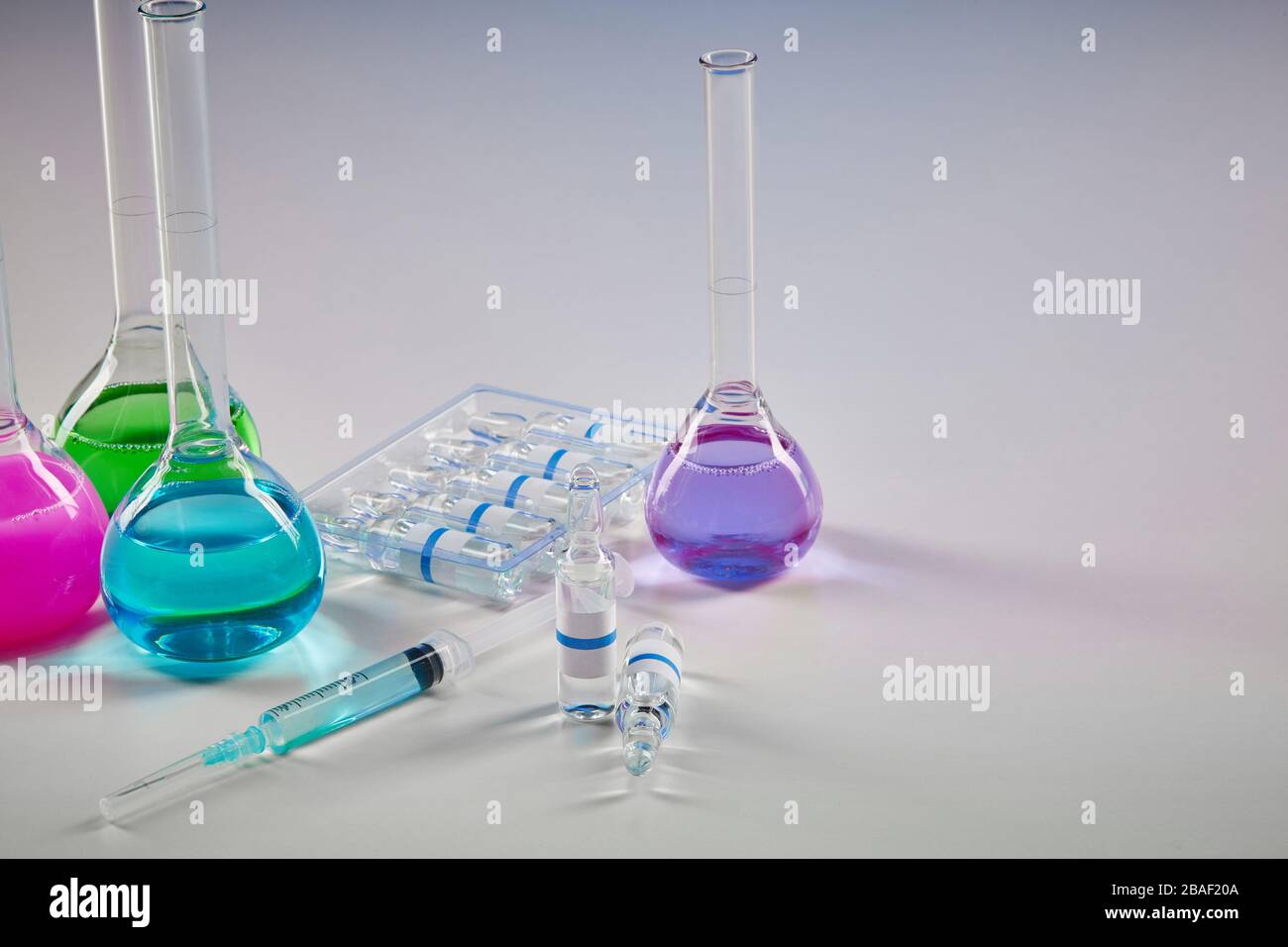 Four medical flasks with colorful chemical reagents. Seven mockup ampoules with transparent liquid and syringe isolated on white. Laboratory research Stock Photo