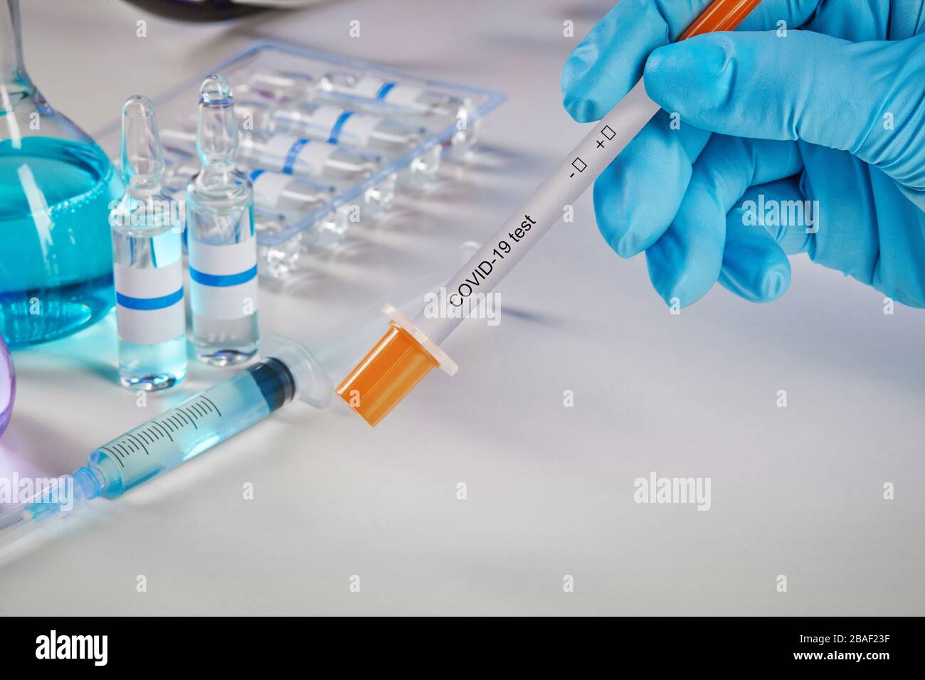 Hands in blue disposable gloves holding testing kit. Medical flasks with colorful chemical reagents. Ampoules with liquid and syringe isolated on whit Stock Photo
