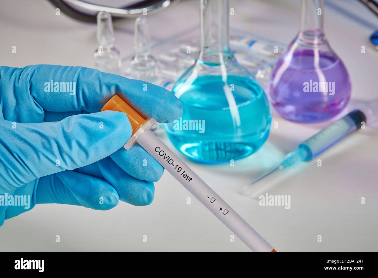 Hands in blue gloves holding testing kit. Medical flasks, colorful chemical reagents. Ampoules with liquid, syringe, phonendoscope isolated on white. Stock Photo
