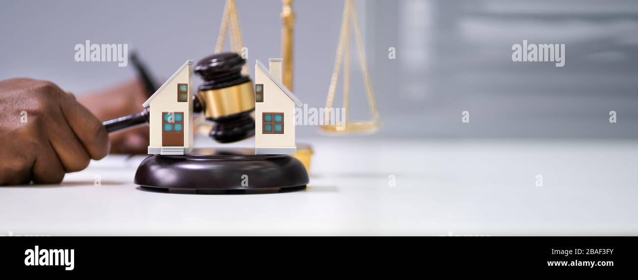 Close-up Of A Judge Striking Gavel Between Split House Over Desk Stock Photo