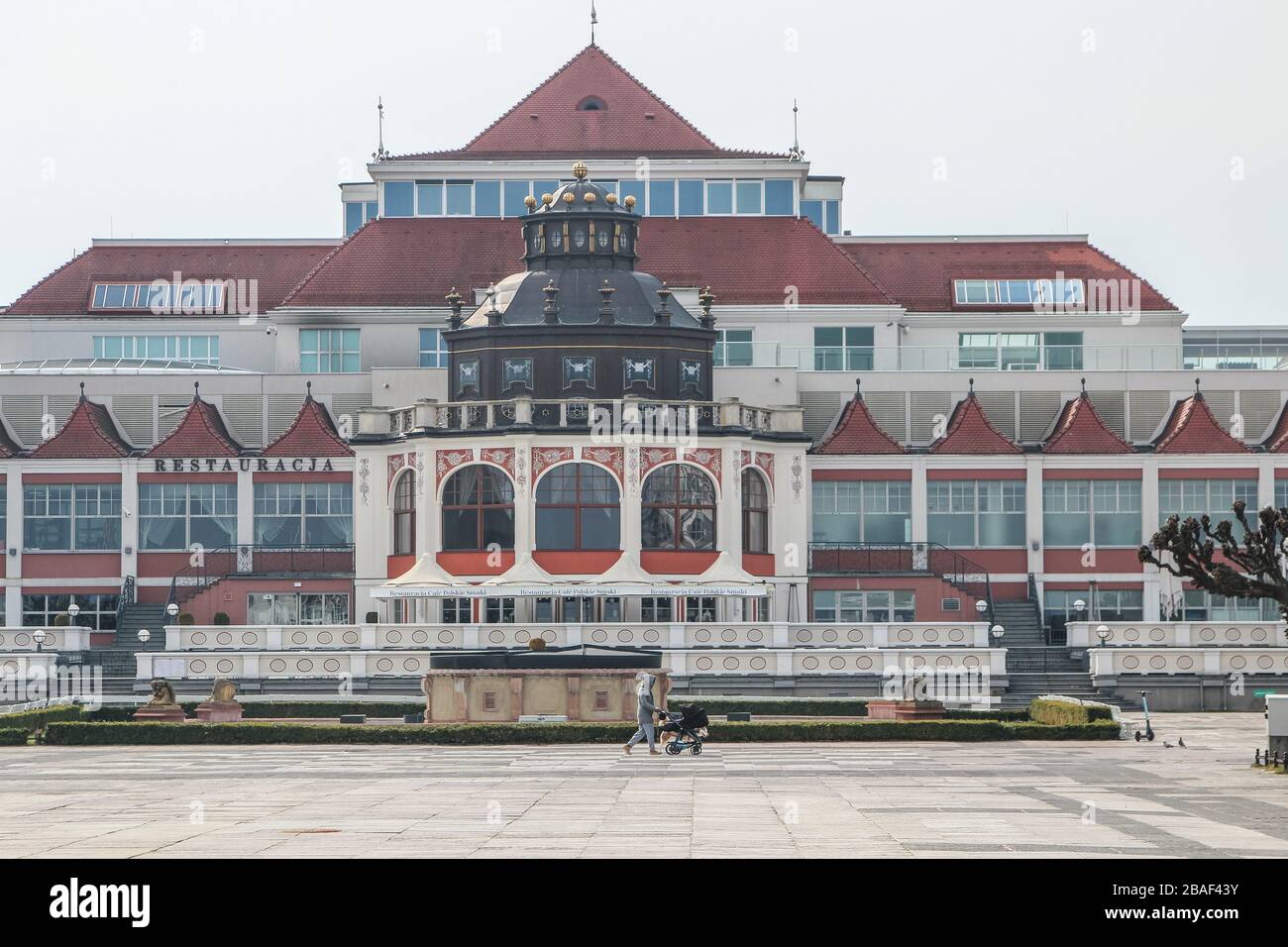 Sopot, Poland. 27th Mar, 2020. Sopot, Poland., . Woman with a trolley walking by the empty Plac Zdrojowy, normally full of people, in front of Grand Hotel is seen in Sopot, Poland on 27 March 2020 Polish government due the Covid-19 danger, forced ban on gatherings of more than 2 people and a ban on leaving home without apparent reason, as for instance going to job, to the pharmacy or for a dog walking. Credit: Vadim Pacajev/Alamy Live News Stock Photo