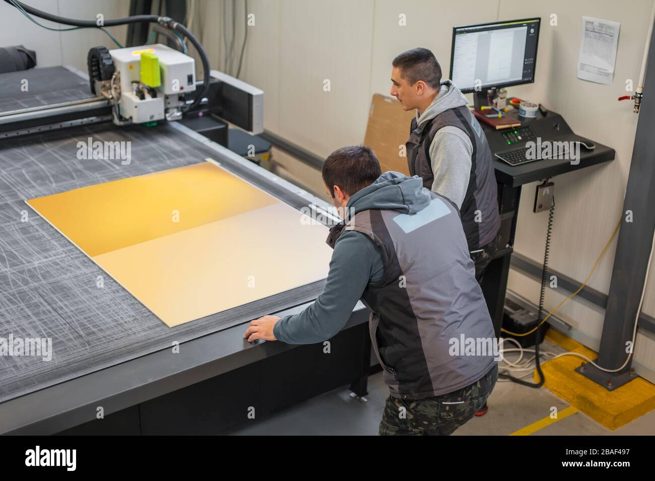 Two printshop worker technicians works on large CNC computer numerical control printing and cutting machine Stock Photo