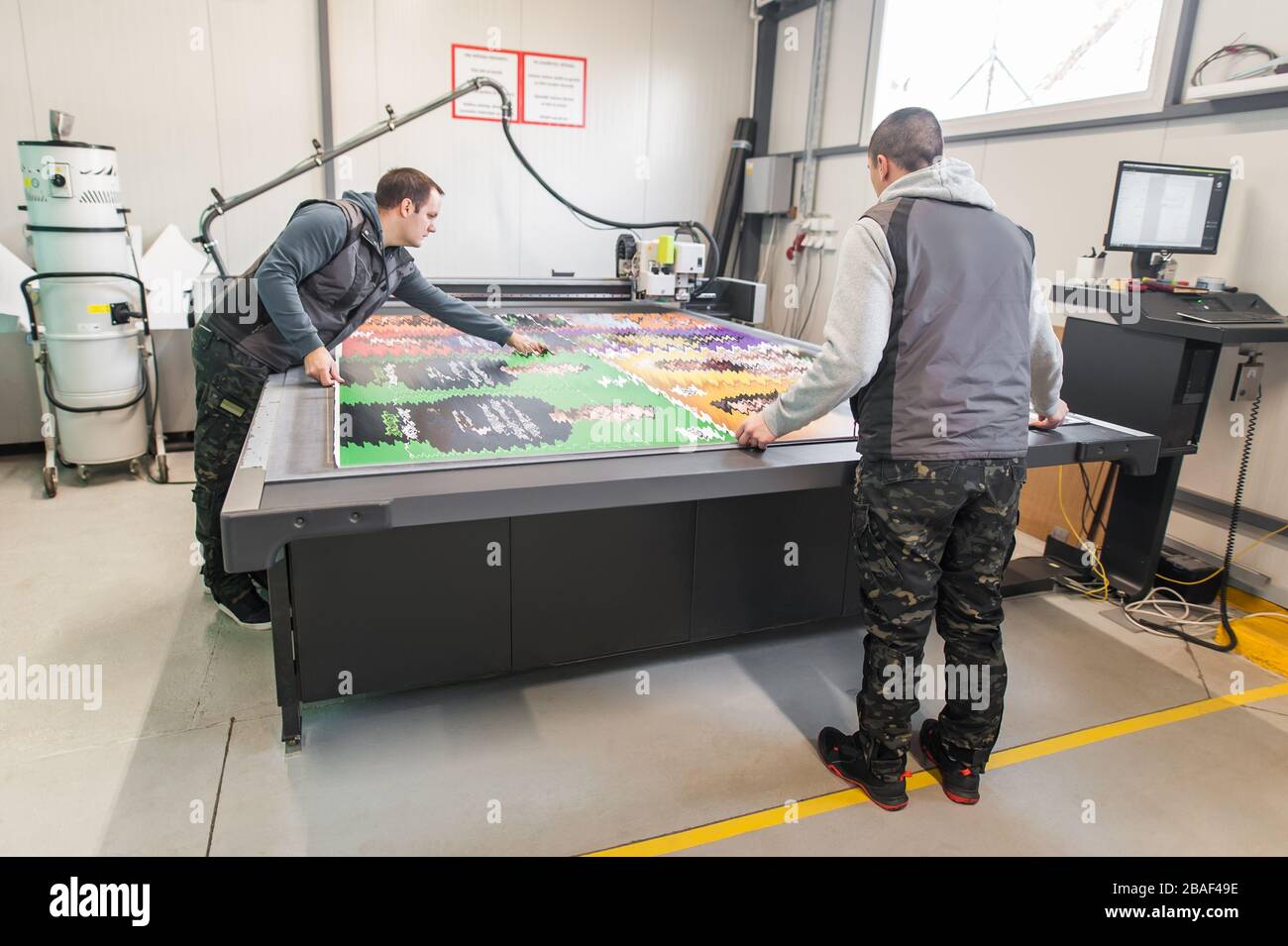 Two printshop worker technicians works on large CNC computer numerical control printing and cutting machine Stock Photo
