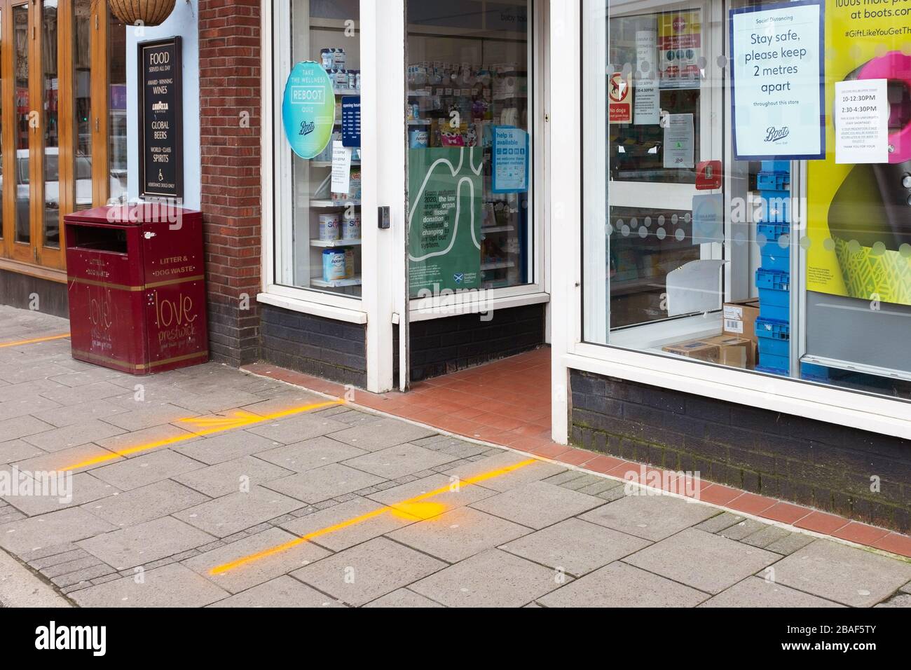 Prestwick, Scotland, UK. 27th Mar, 2020. As the Government's instructions on Covid-19 for self isolation and social distancing become enforceable by legislation and fixed penalty notices, in Prestwick the shopkeepers who remain open ( chemists and food shops) have applied an easy guide for customers to maintain 2 metres safe spacing, by painting guidelines on the pavements. Credit: Findlay/Alamy Live News Stock Photo