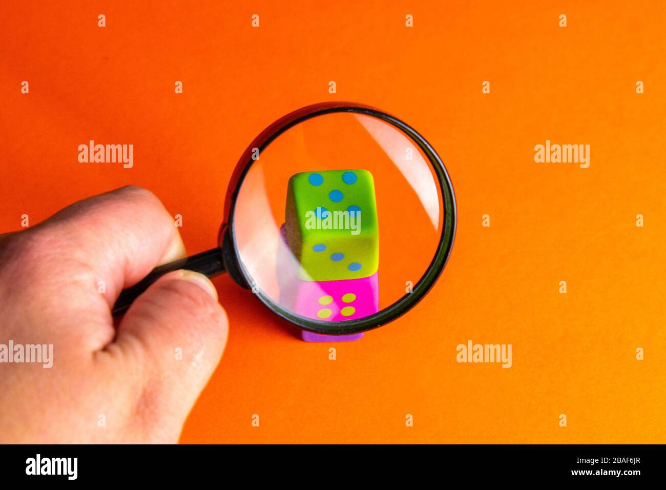 Hand holds magnifying glass over playing cubes. The focus is on the green cube. Search casinos, gambling, fortune Stock Photo