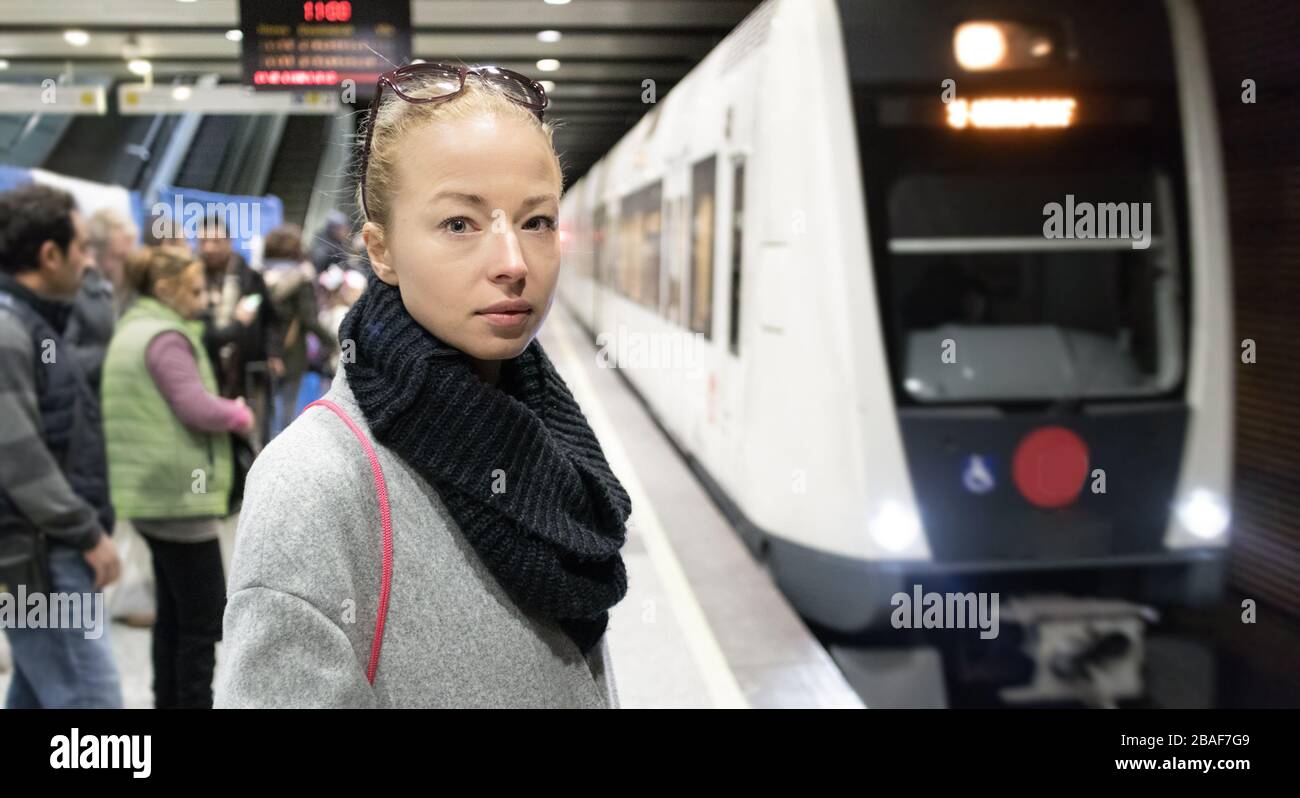 Young woman in winter coat going to work, waiting on the platform of a railway station for train to arrive. Public transport Stock Photo