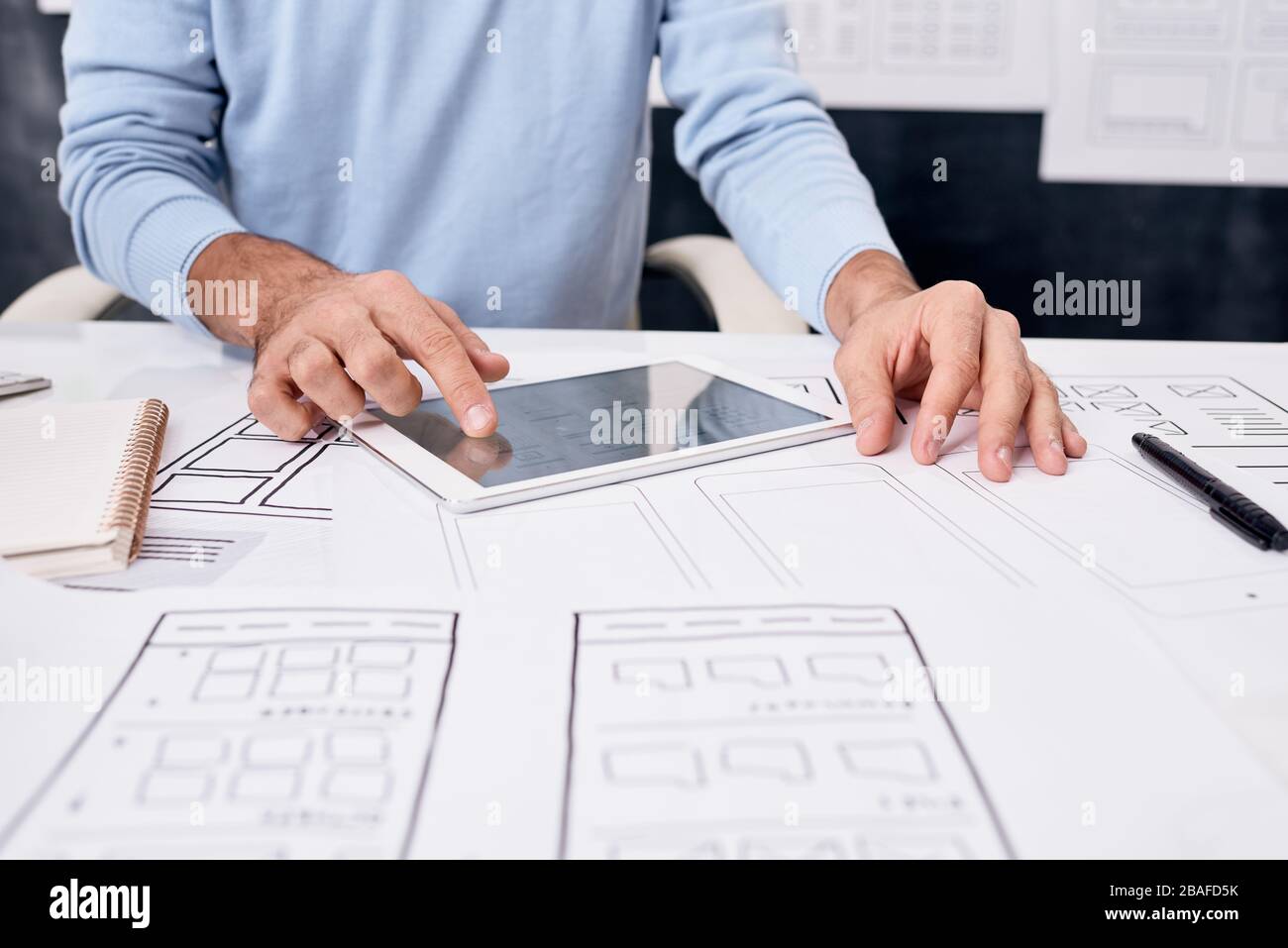 Close-up of unrecognizable man sitting at table with sketches and using tablet while developing app design Stock Photo