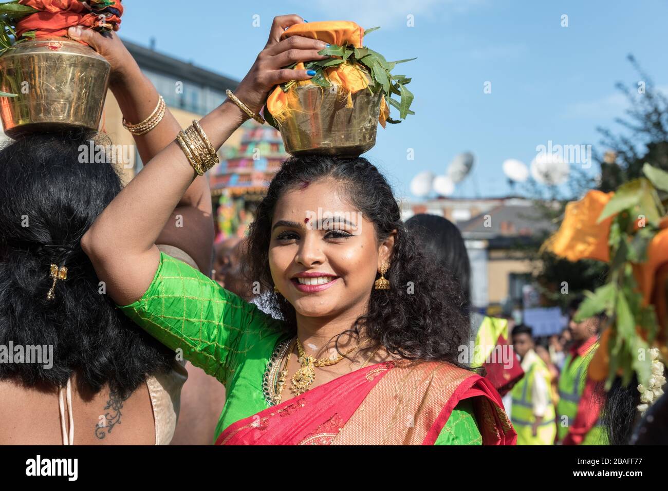 Young Hindu woman in sari, smiling as she participates in a  Chariot Festival procession, carries offering on her head Stock Photo