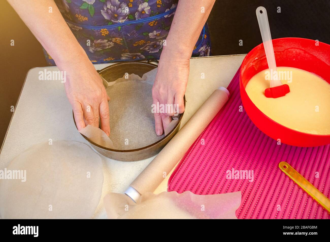 Baking Ingredients and Utensils for Cooking Sponge Cake. Process Cooking Sponge Cake. Woman Puts Parchment Paper on the bottom of the Bakeware. Stock Photo