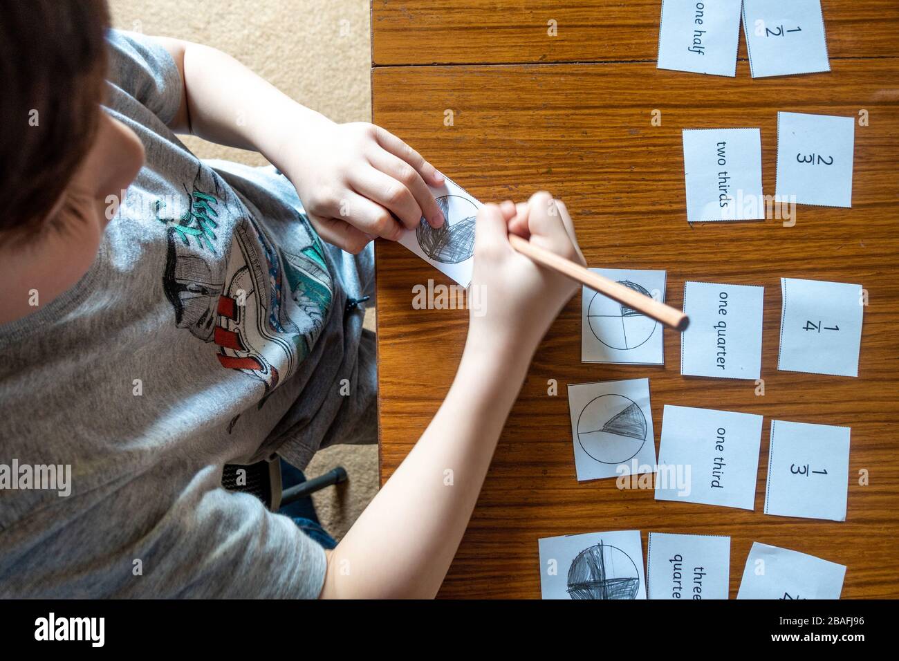 A boy is learning about fractions at home doing maths homework which has been sent during the coronavirus pandemic. Stock Photo