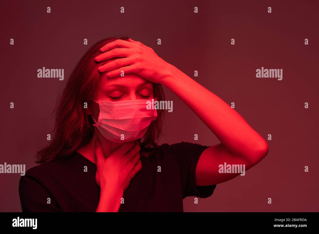 Sick young female in protective mask keeping her hands on forehead and throat while suffering from headache and other symptoms Stock Photo