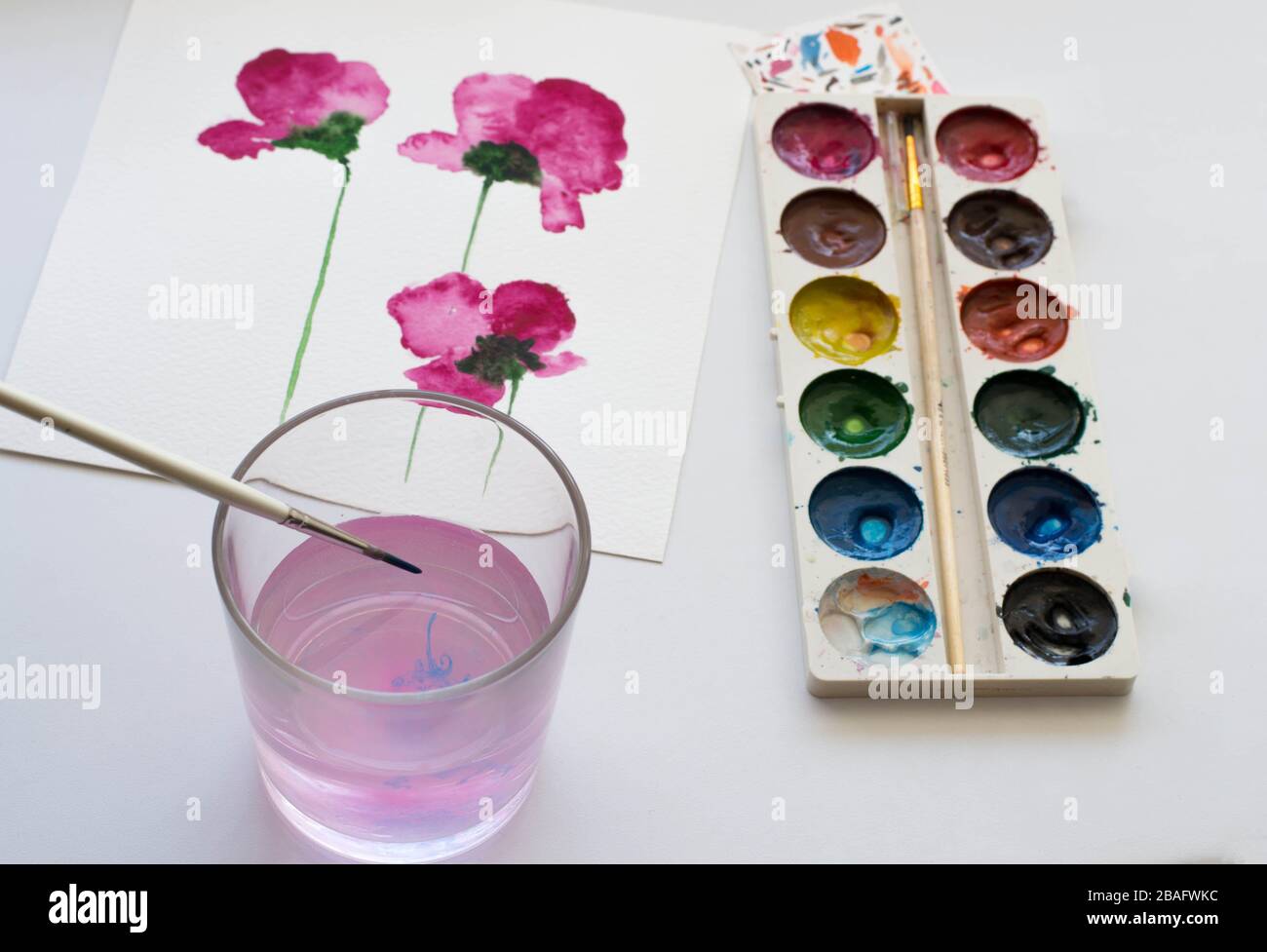 Watercolor painting of pink magnolia flower and artistic tools on white table. Still life composition of artistic workplace Stock Photo