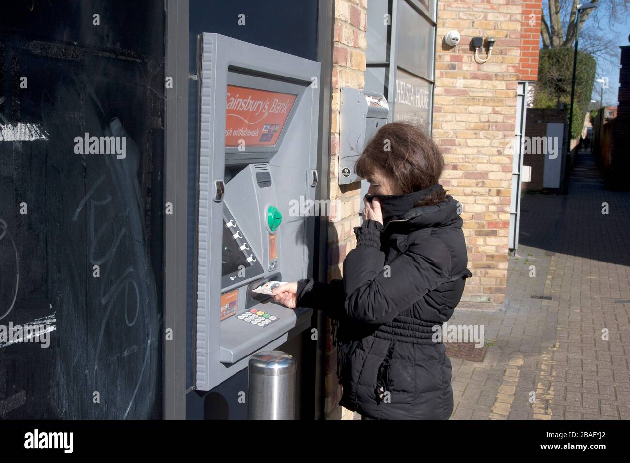 middle aged woman during coronavirus 2020 at ATM covering her face and collecting cash Stock Photo