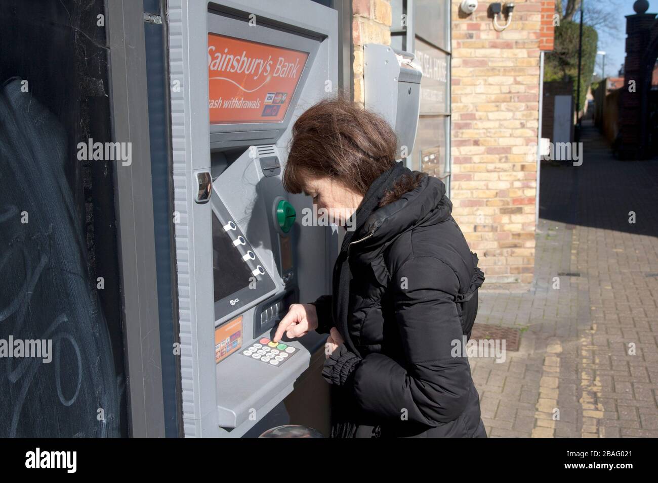 middle aged woman during coronavirus 2020 at ATM pressing keypads Stock Photo