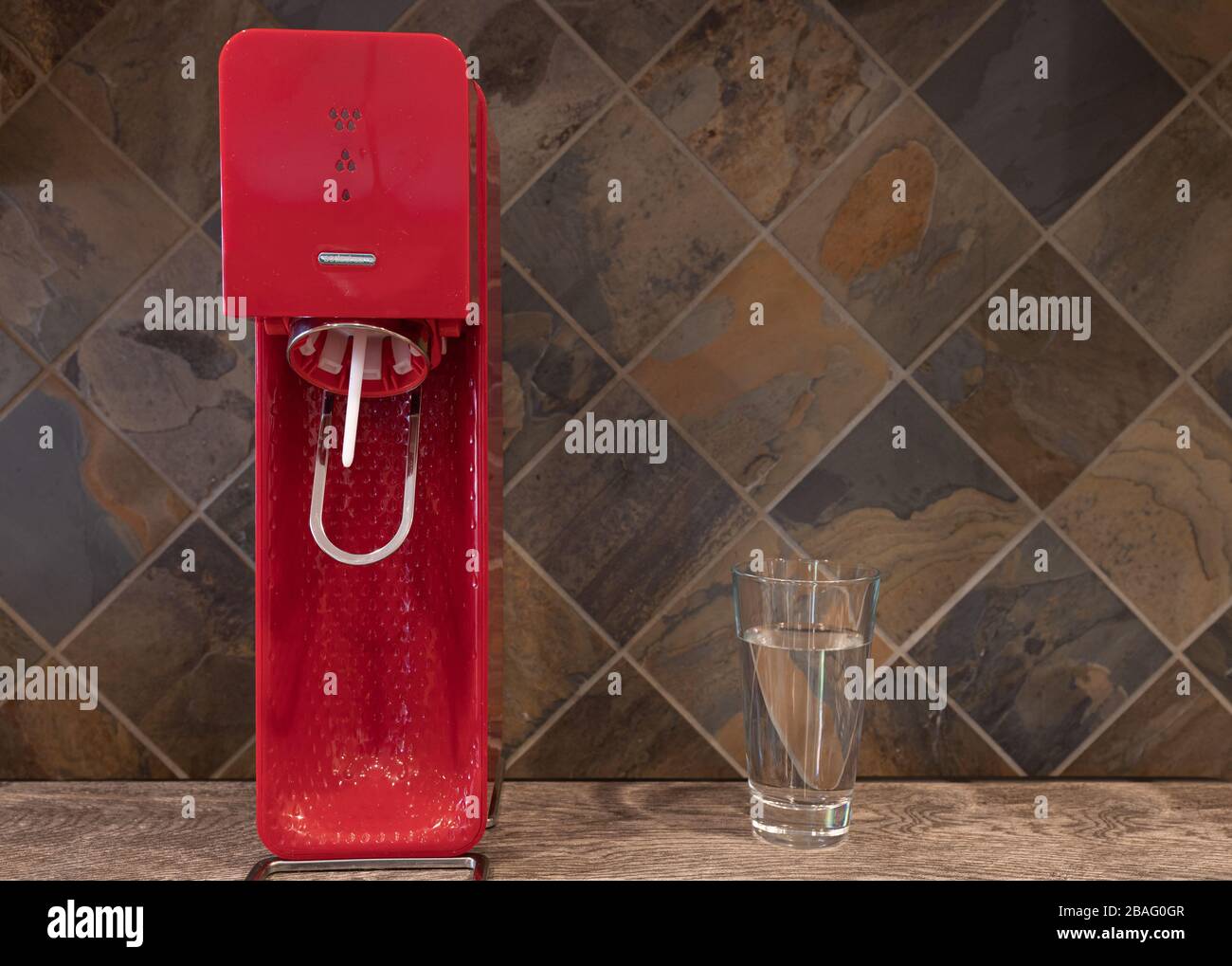 Red Sodastream with Glass of Water in Kitchen with Tile Background Stock Photo