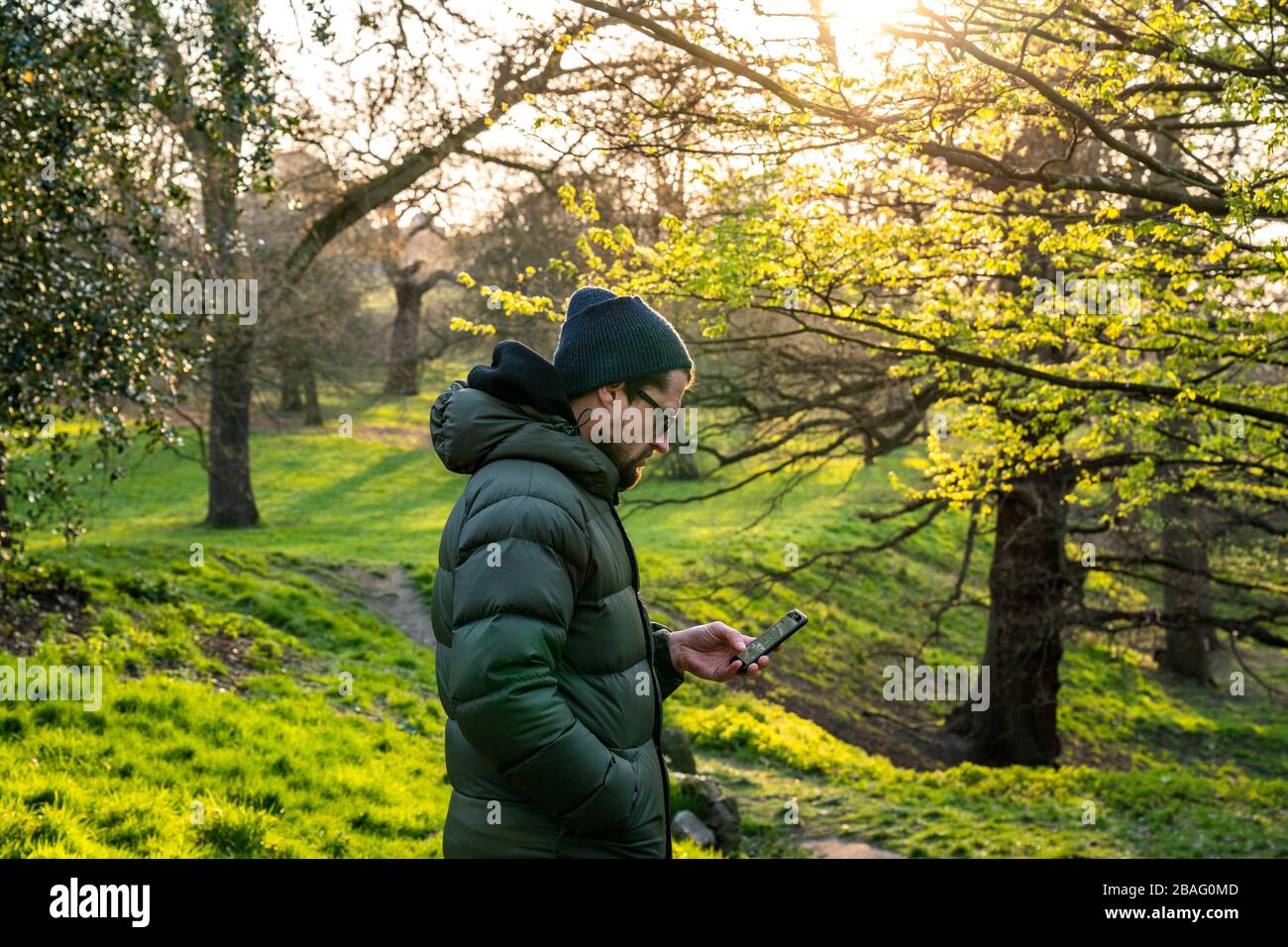 Social distance exercising in Greenwich Park.  Mid 40's male looking at phone. Stock Photo